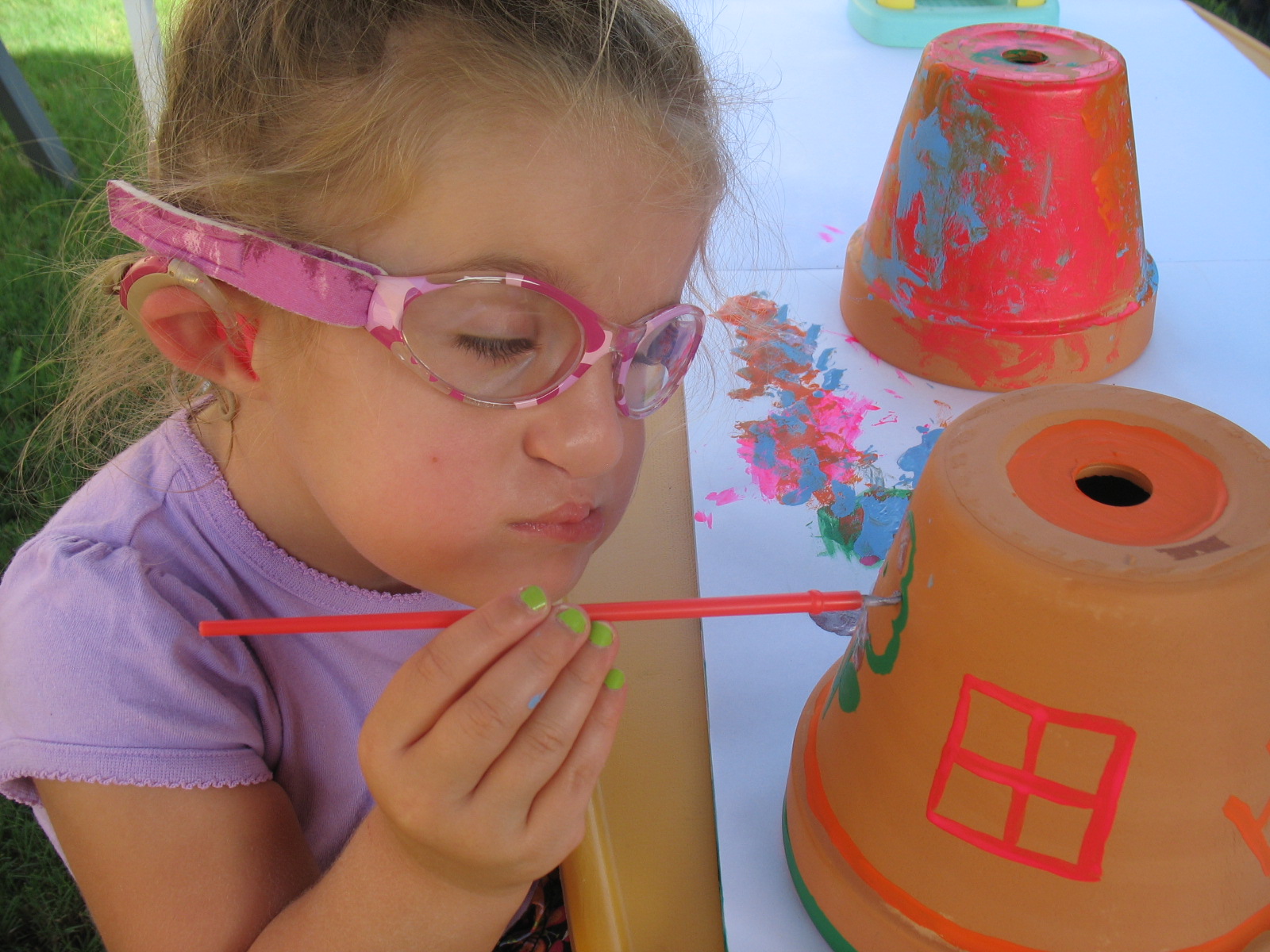 A young girl who is deafblind paints a flowerpot.