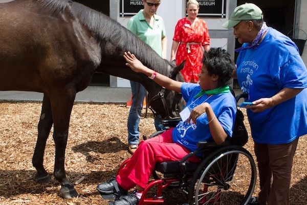 Young woman in wheelchair petting horse.