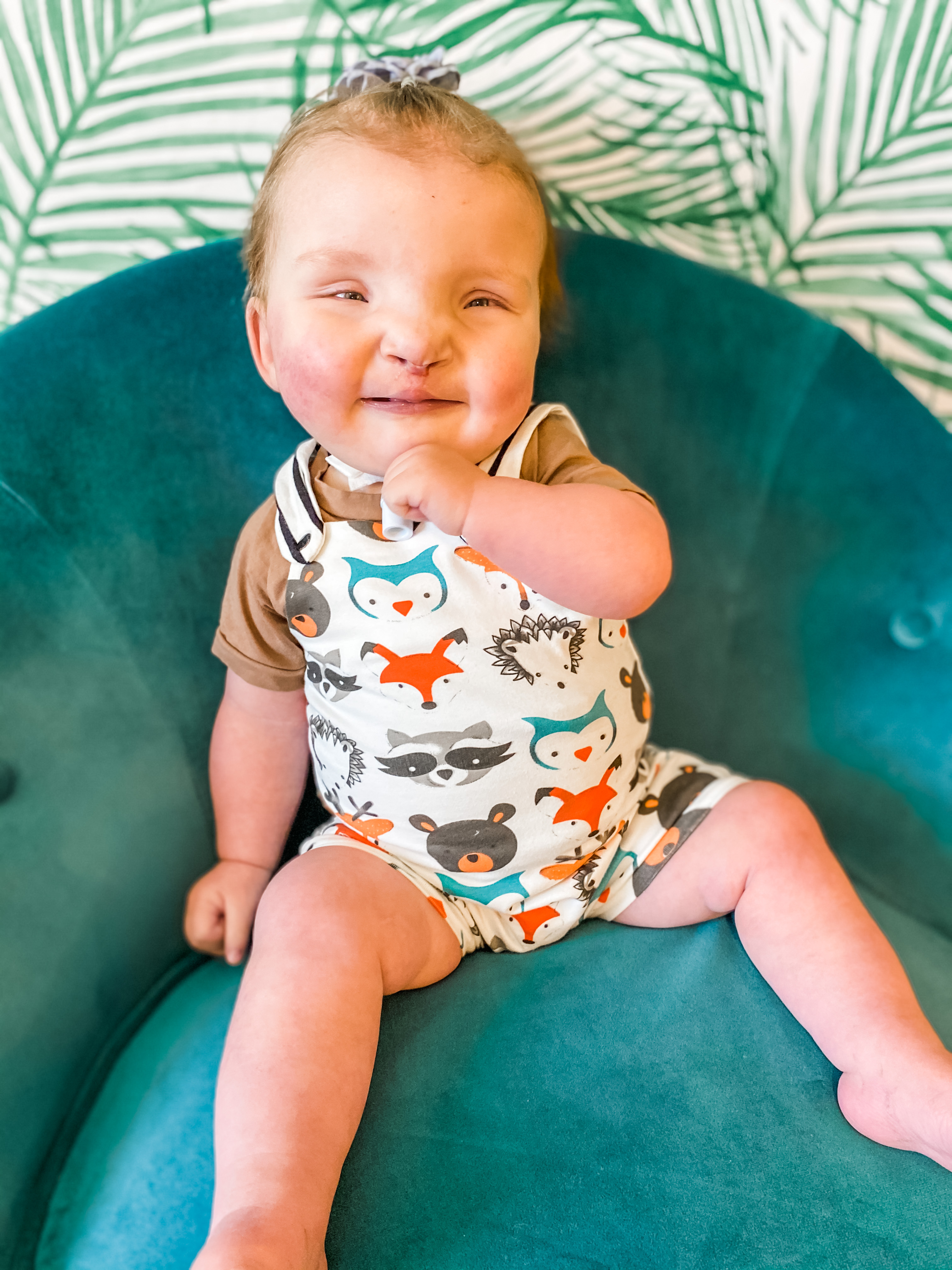 A baby who is deafblind sits on a cushion and smiles. She has a tracheostomy tube.