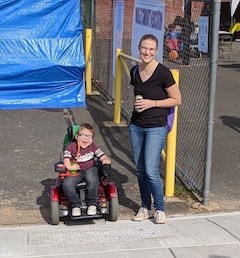 AN intervener stands next to a child in a motorized wheelchair.